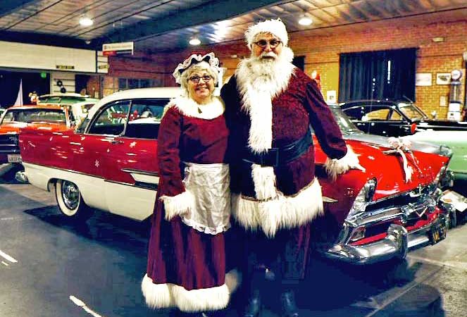 Santa and Mrs. Claus pose for a picture in from of a beautifully restored classic car at the ZADM
